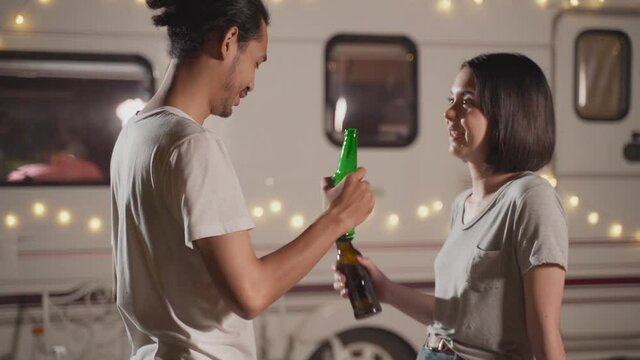 Lovely asian couple clinking, drinking bottles of beer and smiling.