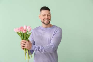 Handsome man with bouquet of beautiful flowers on color background