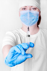 Syringe with sprinkles of medicine in hand of medical worker wearing medical gloves, mask and cap. Focus on the foreground