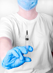 Syringe with sprinkles of medicine in hand of medical worker wearing medical gloves and mask. Focus...
