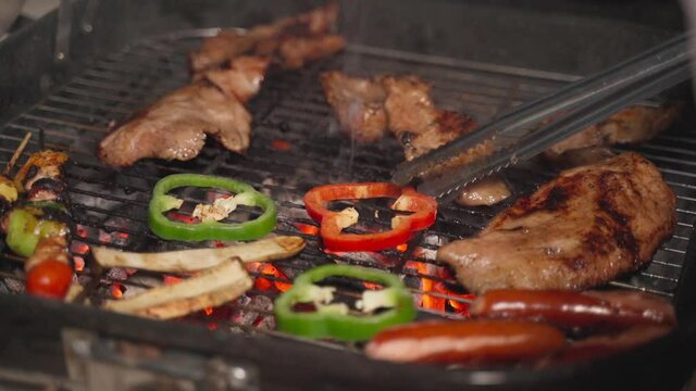 Food tongs holding green and red bell peppers on grill with smoked.