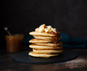 American pancakes with caramel and banana on a dark background