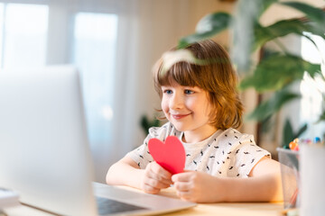 Smiling child boy with Valentine greeting card having a video call chat on laptop, online dating, enjoy holidays at home.