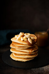 American pancakes with caramel and banana on a dark background, selective focus