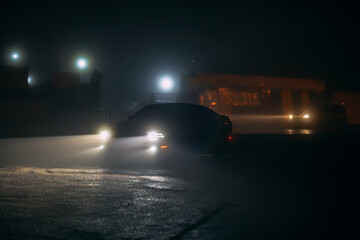 Sport car in the shadows with glowing lights in low light at foggy night, or silhouette of sport...