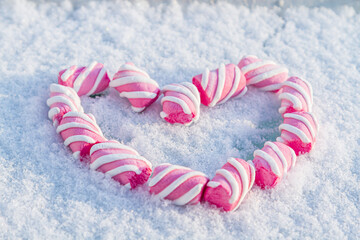 Heart made of marshmallows in the snow. Red heart on a white background. Valentine's Day. Sweets as a gift. Romantic background for Valentine's Day.