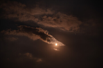 Fototapeta na wymiar first quarter moon on the night sky seen trough brightly clouds during summer season
