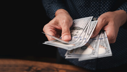 The hand of a business woman counting dollar bills, copy space, black background, money saving...