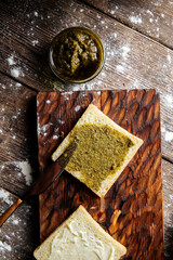 Top view on spreading white bread slice with pesto sauce on the wooden cutting board