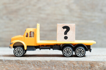 Toy truck hold alphabet letter block question mark on wood background