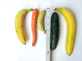 Tape measure and two bananas, one cucumber and one carrot against white background