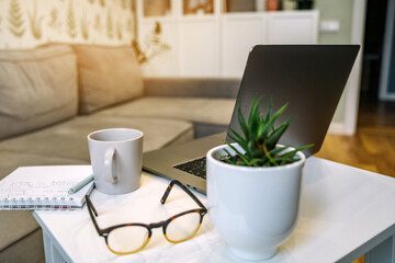 A laptop sits on the coffee table in the living room and a mug of coffee. The concept of remote work from home and online education