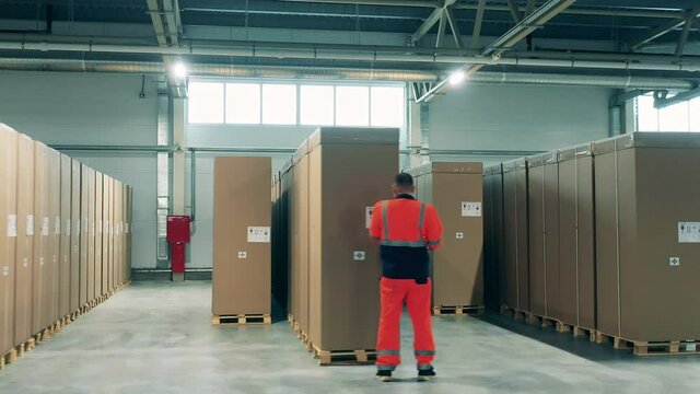 Factory worker is checking boxes with fridges in the warehouse