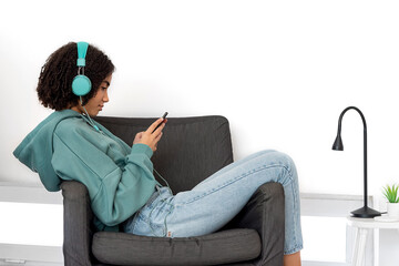 Black teenager in casual clothes browsing smartphone and listening to music while resting in...