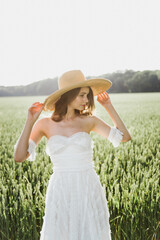 Beautiful young woman in a boho style dress and hat on a field with wheat at sunset.