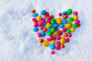 Multi-colored heart shaped candies in the snow. Sweets in the snow. Valentine's Day. Sweets as a gift. Romantic background for Valentine's Day.