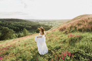 Young beautiful woman in boho style dress and hat on nature at sunset.