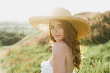 Young beautiful woman in boho style dress and hat on nature at sunset.