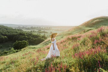 Young beautiful woman in boho style dress and hat on nature at sunset.