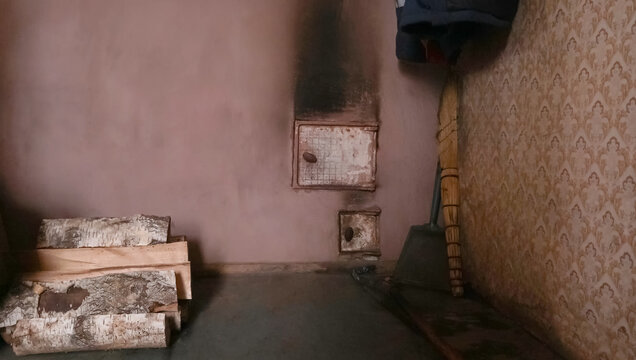 Gray clay stove in the old house of my grandmother in the village, next to the firewood, there is a broom and a shovel