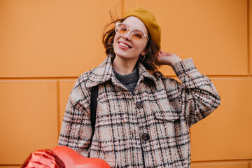 Positive girl in tweed coat with smile posing on orange background. Lady in sunglasses and mustard...