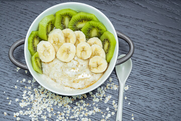 Oatmeal porridge with bananas, kiwi in in a bowl on a dark background, top view. Healthy breakfast