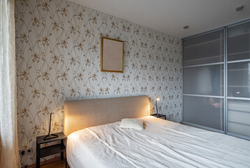 Contemporary interior of bedroom in luxury flat. Cozy bed. Huge sliding door wardrobe. Lamp on nightstand.