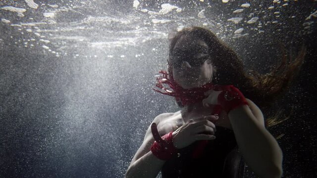 sexy lady with red whip is swimming underwater in bubbles and light, mysterious and magic shot