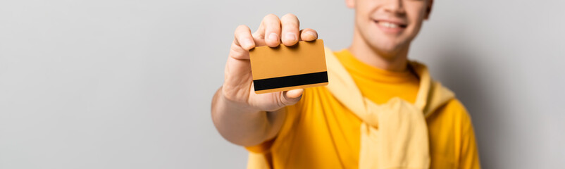 Cropped view of credit card in hand of young man blurred on grey background, banner