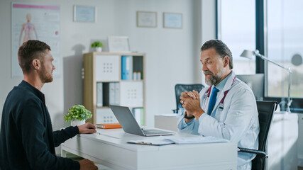 Family Doctor is Delivering Great News About Male Patient's Medical Results During Consultation in a Health Clinic. Physician in White Lab Coat Sitting Behind a Computer in Hospital Office. 