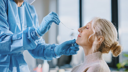 Medical Nurse in Safety Gloves and Mask, Protective Face Shield and Overalls is Taking a PCR Corona Virus Sample in a Health Clinic. Doctor Uses Respiratory Swab Test. Covid-19 Pandemic Concept.