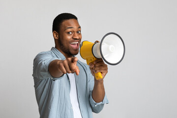 Positive african guy shouting in megaphone over grey background - obrazy, fototapety, plakaty