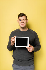 Smiling man holding digital tablet with blank screen on yellow background