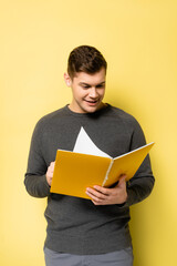 Smiling man looking at notebook on yellow background