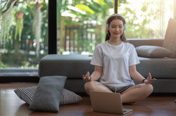Asian woman interested in yoga by opening the laptop to listen to yoga practice music at home.