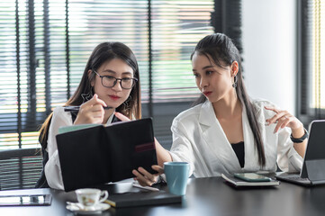 Obraz premium Two young asian business woman are working on a new project. by taking notes and using a tablet at office.