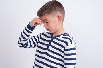 Very upset, little cute boy kid wearing red stripped t-shirt against white wall touching nose...