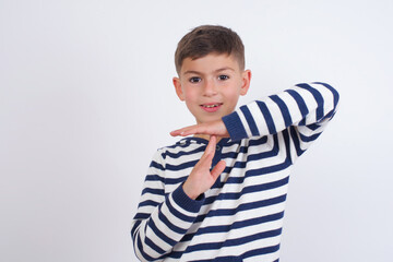 little cute boy kid wearing red stripped t-shirt against white wall feels tired and bored, making a timeout gesture, needs to stop because of work stress, time concept.