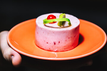 Delicious piece of cake on a plate in hands on a dark background