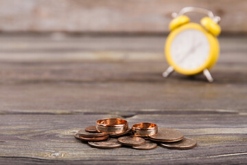 Wedding rings and pile of coins. Alarm clock on the background.