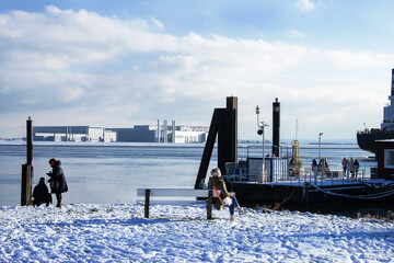 Groups of unrecognizable people from the back having a rest on the bank of the elbe in hamburg on a sunny winter day