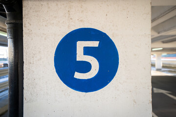 White coloured hand painted level number five in the middle of a blue colour circle painted on an old textured concrete pillar wall