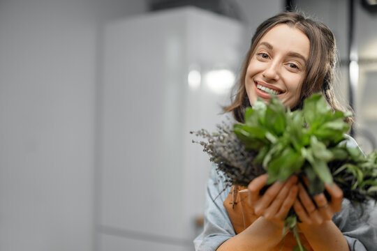 Portrait of cheerful woman in apron with fresh spicy herbs basil, rosemary, thyme on the kitchen. Healthy cooking concept. Close up. Image with copy space. High quality photo