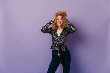 Charming European girl in elegant silver blouse laughs and disarranges her hair against purple background