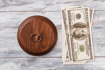 Top view dollars bills and wedding rings. White wood background.