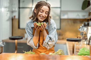 Portrait of pretty woman in apron with fresh brussels sprouts on the kitchen at home. Healthy cooking concept. High quality photo