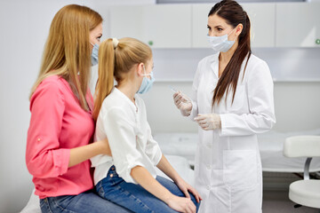 Fototapeta premium female doctor preparing child before making injection, consulting. girl sits with mother in hospital listening to nurse talks