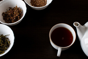 a cup of tea and various types of dried tea to make on a black background