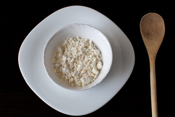 cottage cheese in a white plate and a wooden spoon on a dark background