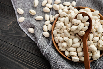 Pistachios in a wooden spoon. Wooden bowl with nut pistachios. on a wooden background, near a bag from burlap. Healthy food and snack, organic vegetarian food. (selective focus; close-up shot)